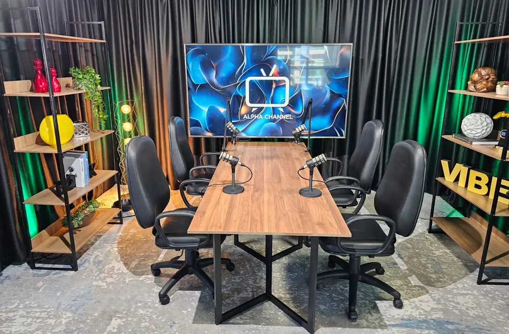 Cenário de mesacast do estúdio da Produtora 76, com mesa, quatro cadeiras e microfones